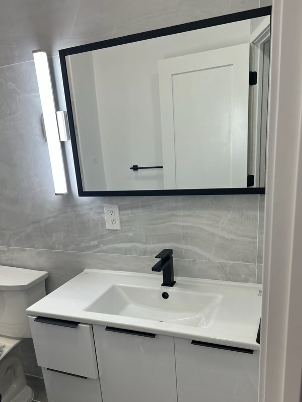 Floating white vanity with black matte faucet, framed mirror and marble-look tile surround &mdash; Huntington, NY